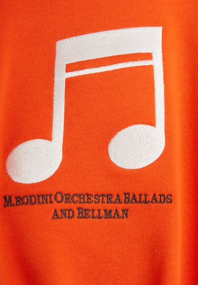 Oranžová tkanina s veľkým bielym dizajnom hudobnej noty, doplnená čiernym vyšívaným textom "Mrodini Orchestra Ballads and Bellman."