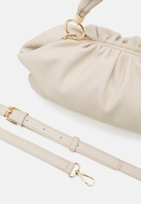 Béžová kožená taška se shromážděným designem, zlatými detaily a odnímatelným popruhem. Hladká textura, zaoblený tvar, minimalistický styl.