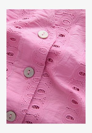 Pink fabric featuring intricate lace detailing and alternating circular cutouts, with round, pearl-like buttons along the front.