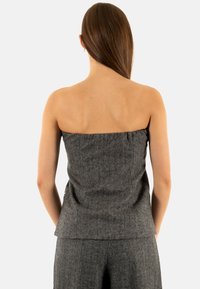 Top senza maniche a spina di pesce grigia con un corpetto aderente e dettaglio peplum in vita, realizzato in tessuto testurizzato. Design della schiena semplice.