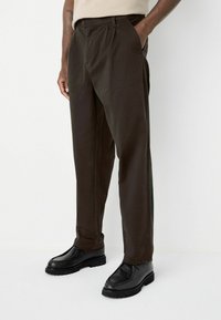 Dark brown trousers made of cotton fabric, featuring a straight-leg design and side pockets, paired with black lace-up shoes.