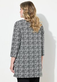 Zwart-witte tuniek met een gevlekt patroon, driekwart mouwen, een ronde halslijn en een iets langere achterkant.