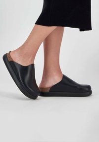 Black closed-back clogs with a smooth leather upper, cork accent at the heel, and a textured black rubber sole.