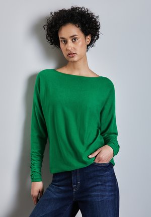 Groene lange mouwen top met een boot-halslijn, voorzien van een zachte textuur en aansluitende mouwen, gecombineerd met donkerblauwe denim jeans.