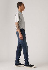 Gray short-sleeve t-shirt, blue denim jeans, and black sneakers. Side view, showing a smooth, fitted shape and subtle textile texture.