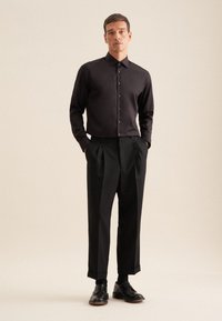 Camicia nera con bottoni realizzata in tessuto morbido, abbinata a pantaloni neri a vita alta e scarpe nere stringate. Design minimalista.