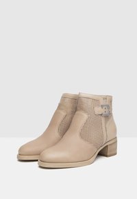 Stivaletti beige in pelle con lati perforati, tacco blocco basso e un accento argentato sulla caviglia esterna per un tocco di originalità.