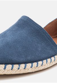 Blue suede slip-on shoe with a rounded toe, featuring a woven jute sole and contrasting blue stitching along the edge.