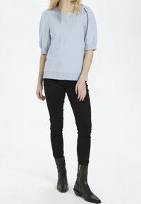 Světle modré tričko s krátkým rukávem, kulatým výstřihem a nabíranými rukávy, v kombinaci s černými slim-fit kalhotami a černými kotníkovými botami.