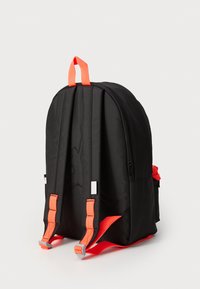 Sac à dos noir avec des sangles et une poignée orange, ayant une texture lisse, des compartiments zippés et une forme rectangulaire.