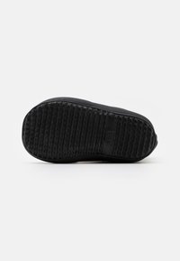 Semelle de chaussure noire avec un motif texturé et un bout arrondi. Le matériau semble en caoutchouc, avec un bord lisse et un branding minimal.