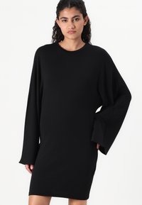 Čierne oversized šaty s dlhými rukávmi, okrúhlym výstrihom, vyrobené z hladkej textílie, po kolená, s voľným strihom.