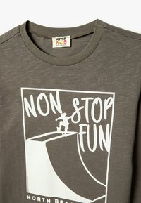 Szary bawełnowy T-shirt z białą grafiką deskorolkarza oraz napisem "NIEUSTAJĄCA ZABAWA" i "PÓŁNOCNA PLAŻA" na dole.