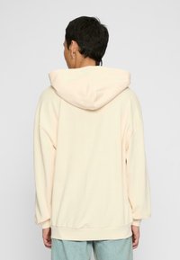 Oversized cream hoodie with a drawstring hood, ribbed cuffs, and hem, featuring a soft texture and relaxed fit.