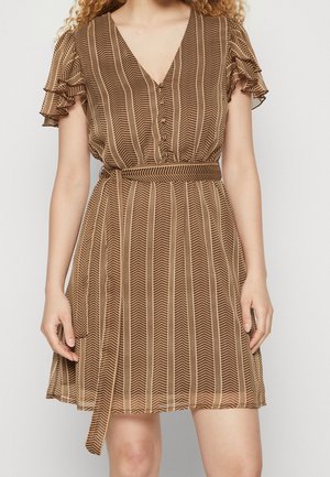 Vrouw draagt een bruine jurk met korte mouwen, verticale chevronstrepen, gerimpelde mouwen, V-hals en een bijpassende stoffen riem gestrikt in de taille.