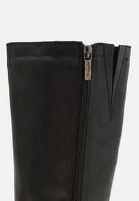 Botín negro de cuero hasta el tobillo con cremallera lateral, que presenta una textura suave y detalles de costura a lo largo del borde y la línea de la cremallera.