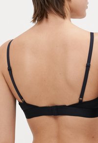Soutien-gorge noir avec des bretelles fines et ajustables, un design sans couture et une fermeture à crochet au dos. Texture lisse et construction simple.
