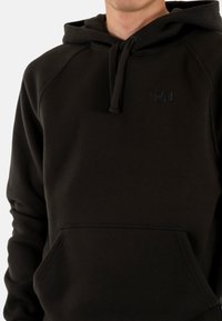 Felpa con cappuccio in tessuto nero con tasca a marsupio, caratterizzata da un logo discreto. Superficie texturizzata, maniche raglan in stile sportivo.