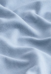 Světle modrá látka s texturovaným vzorem malých, rovnoměrně rozmístěných teček. Materiál vypadá měkce a mírně reflexně, s jemnými záhyby.