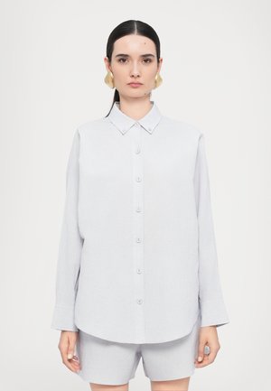 Camicia grigia chiara a maniche lunghe con collo alla francese e orlo arrotondato. Il tessuto appare morbido; presenta bottoni abbinati e una vestibilità rilassata.