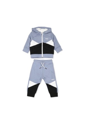 Ensemble de survêtement en deux pièces de couleur bleu clair, comprenant une veste à capuche zippée avec des accents géométriques noirs et blancs et un pantalon de survêtement assorti avec cordon de serrage.