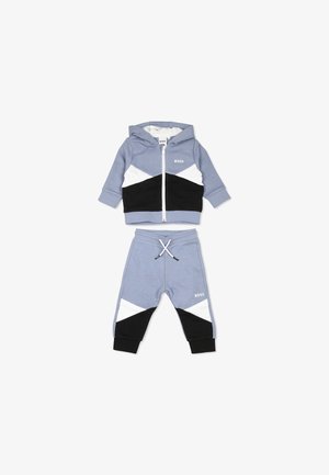 Completo tuta a due pezzi di colore azzurro chiaro, composto da una giacca con cappuccio e zip, arricchita da accenti geometrici in bianco e nero, e pantaloni della tuta abbinati con cordoncino.