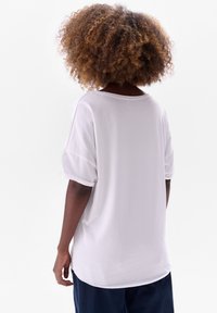 Witte oversized t-shirt met een brede halslijn en opgerolde korte mouwen. Glad stof met een ontspannen pasvorm, gezien vanuit de achterkant.