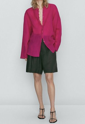 Personne portant un chemisier ample magenta boutonné, un short noir à hauteur des genoux et des sandales noires à talons hauts avec des brides.