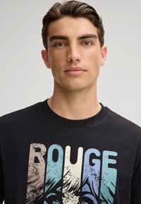 Zwarte katoenen t-shirt met het woord "ROUGE" in gradient kleuren, voorzien van een versleten textuur en een grafisch ontwerp van een gezicht.