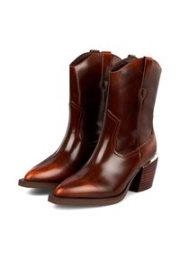 Botas de ante marrón con puntera afilada, paneles laterales y un tacón apilado con un acento dorado. Textura suave con costuras mínimas.
