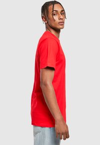 Camiseta de algodón roja con cuello redondo, mangas cortas y corte recto, combinada con vaqueros de color azul claro para un look informal.
