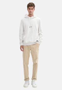 Sudadera gris claro con un bolsillo frontal y cordones, combinada con pantalones beige arremangados y zapatillas blancas. Textura de tela suave.