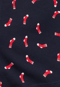 Granatowa tkanina z powtarzającym się wzorem małych czerwonych skarpetek z białymi końcówkami i paskami, oferująca zabawny i teksturowany design.