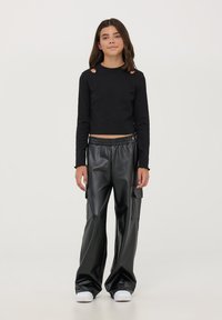 Czarny krótki top z długim rękawem i wycięciami na ramionach, w zestawie z czarnymi spodniami o szerokich nogawkach z sztucznej skóry, z bocznymi kieszeniami. Białe sneakersy.