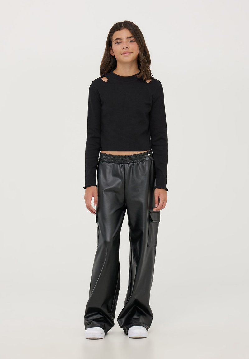 Czarny krótki top z długim rękawem i wycięciami na ramionach, w zestawie z czarnymi spodniami o szerokich nogawkach z sztucznej skóry, z bocznymi kieszeniami. Białe sneakersy.