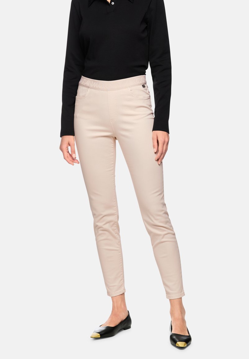 Beige fitted pants with an elastic waistband, front pockets, and a smooth texture, paired with black flats featuring gold accents.