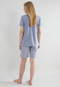 Maglietta azzurra a maniche corte abbinata a pantaloni corti a quadri in tonalità di blu e bianco, che mostrano una vestibilità rilassata e un tessuto morbido.