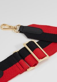 Cinghia intrecciata rossa e nera con clip e fibbia in metallo tono oro; presenta un accento in pelle nera liscia vicino al punto di attacco.