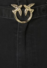 Svart tyg med en texturerad yta har en gyllene cirkulär spänne prydd med två fågelmotiven, vilket ger en dekorativ accent.