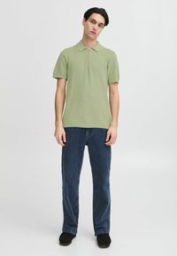 Lys grønn kortermet polo skjorte med et strukturert strikkemønster og glidelås i kragen, kombinert med mørkeblå rette jeans.