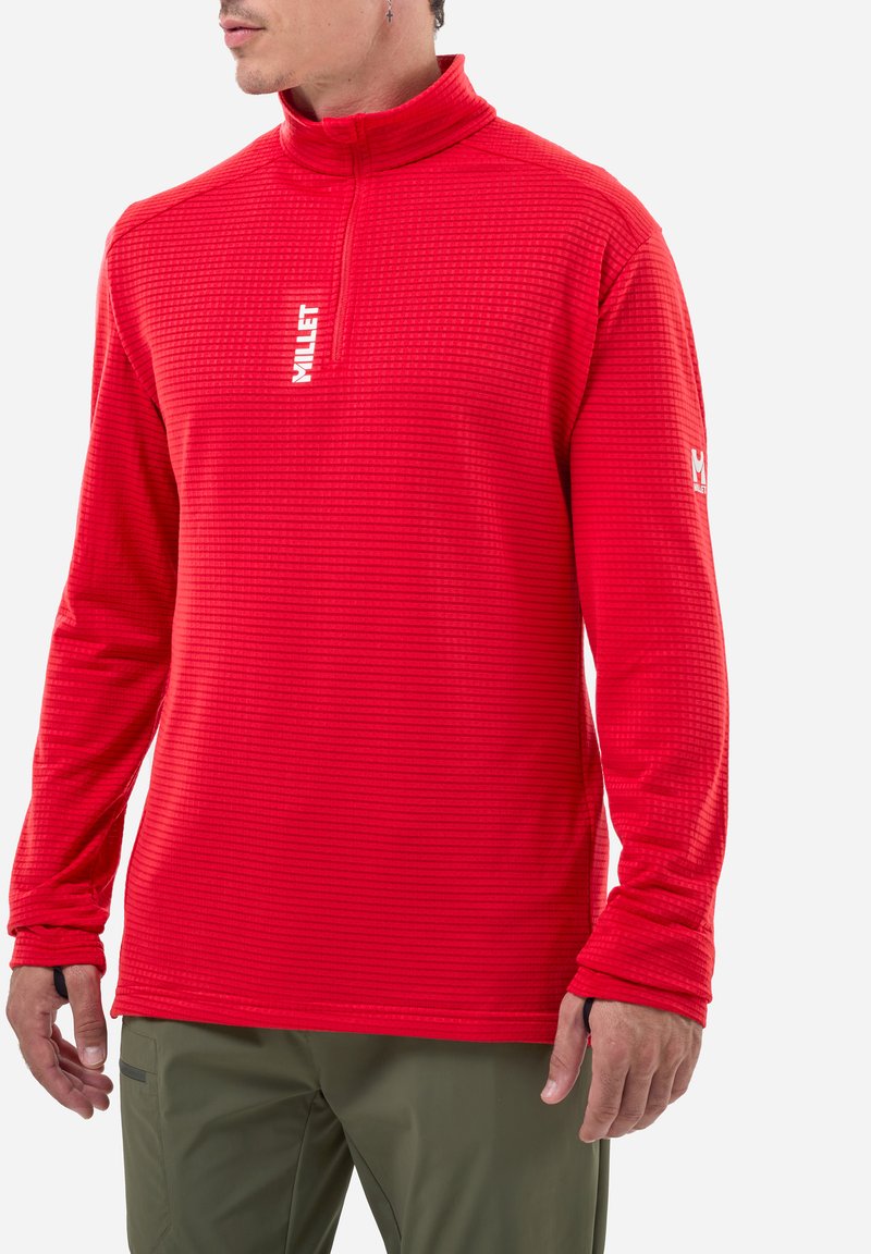 Red long-sleeve pullover with a half-zip collar, textured fabric, and logo detail on the chest and sleeve; fitted design with stretch.