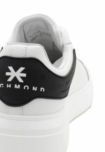 Baskets blanches avec un talon en cuir noir, présentant un logo blanc et une semelle épaisse. Tige en synthétique lisse avec un col rembourré.