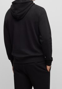 Zwarte hoodie met een zachte textuur, een capuchon met trekkoord en manchetten. Gecombineerd met bijpassende zwarte broek met zijzakken. Eenvoudig ontwerp.