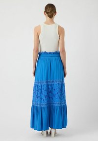 Blauwe maxi rok met een gelaagde ontwerp met kantdetails aan de onderrand en een ontworpen tailleband, gecombineerd met een aansluitend wit tanktop.