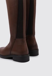 Botas de cuero marrón hasta la rodilla con paneles laterales elásticos, punta redonda, superficie texturizada y suela de goma baja para mayor estabilidad.