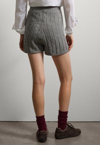 Shorts de punto gris con textura acanalada, cintura alta y una silueta ligeramente ajustada. Combinados con calcetas burdeos y zapatos marrones.