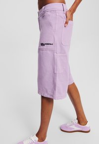 Lavanda cargo kratke hlače izrađene od pamučnog materijala, s bočnim džepovima i crnim logotipom. Uparene s svijetlopurple tenisicama.