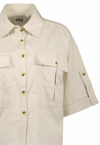Camisetta beige a maniche corte realizzata in cotone, con due tasche sul petto, bottoni gialli, colletto classico e un design dalla vestibilità rilassata.