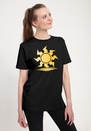 Zwarte katoenen t-shirt met een grote gele zonafbeelding met spitse stralen en een cirkelvormig midden, weergegeven op een neutrale achtergrond.