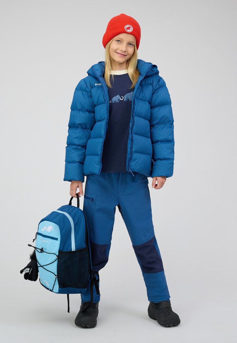 Blauer Pufferjacke, marineblauer Sweatshirt mit Elefantengrafik, blaue Hose, roter Strickmütze, schwarze Winterstiefel und hellblauer Rucksack mit Akzenten.